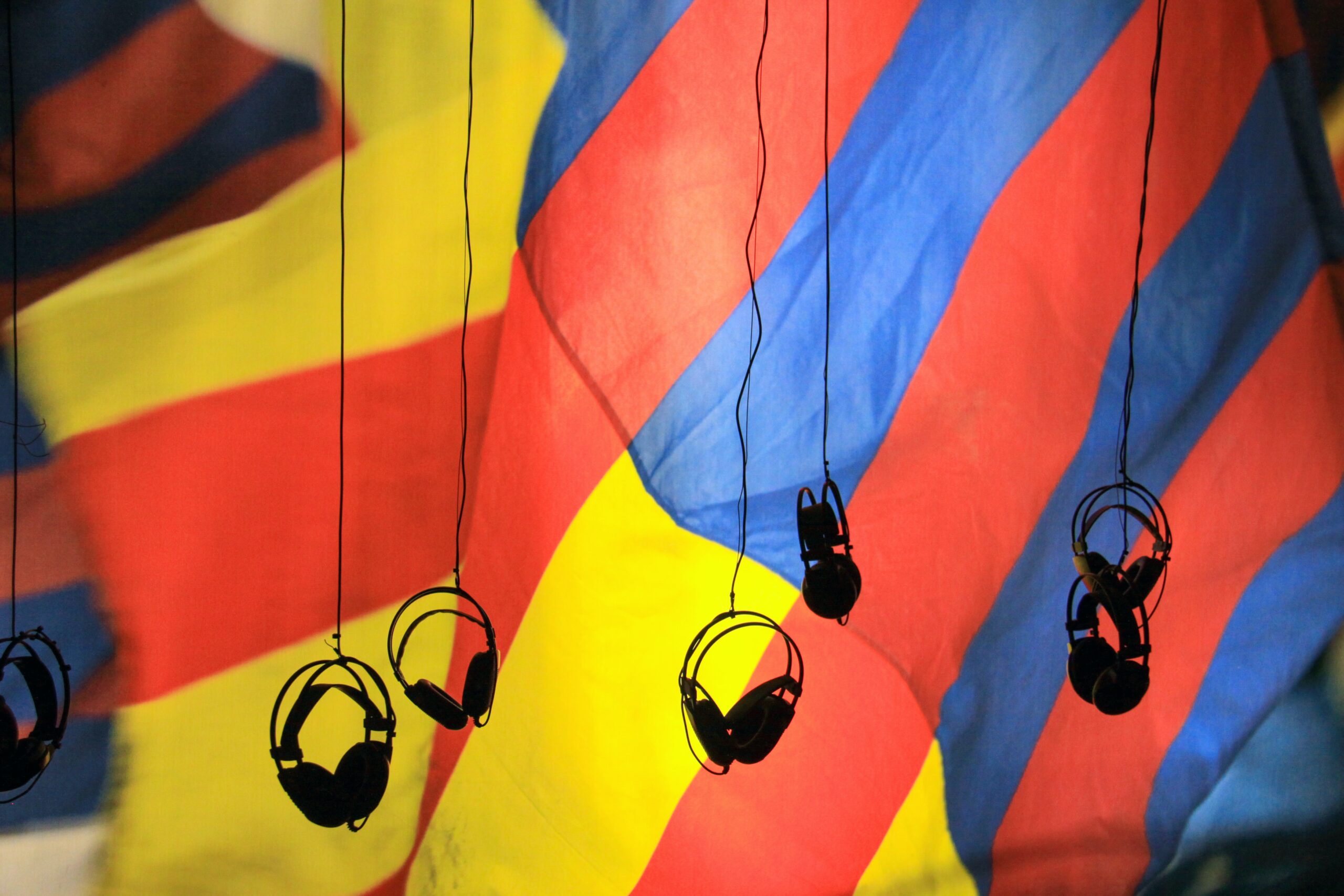 A red, yellow and blue striped flowing background with 6 headphones hanging from the ceiling.